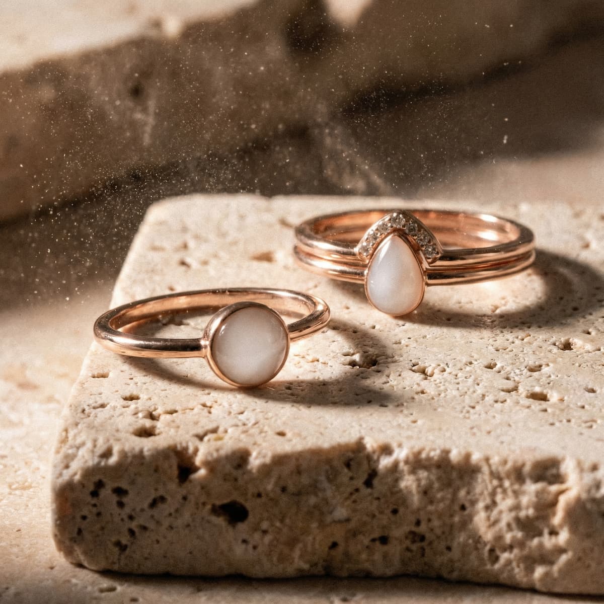 Dos anillos de oro rosa con piedra blanca estilo leche materna sobre base de piedra con luz cálida, ejemplo de anillo leche materna diy.