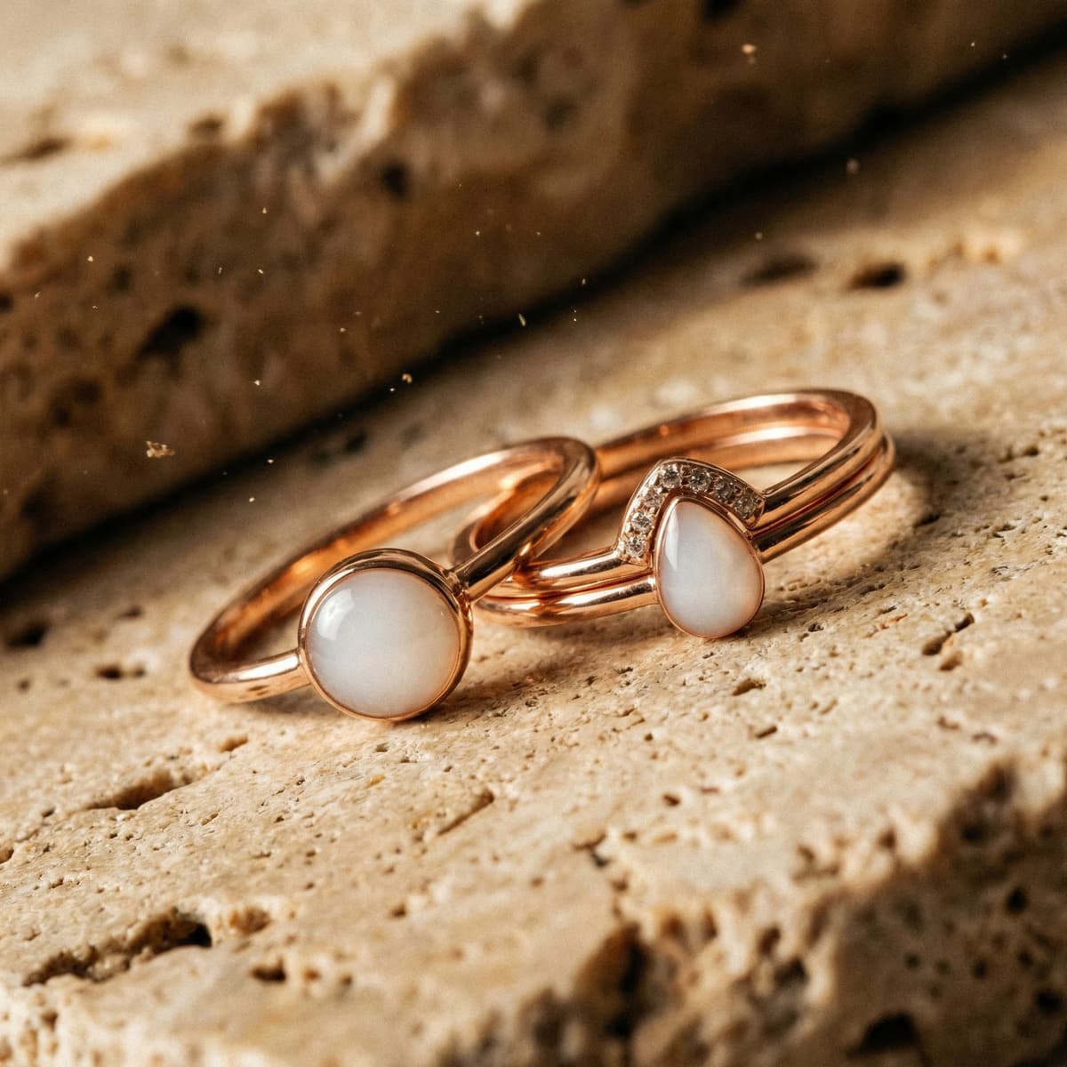 Dos anillos de lactancia DIY en oro rosa con cabujones blancos tipo leche materna, fotografiados en primer plano sobre una superficie de piedra.