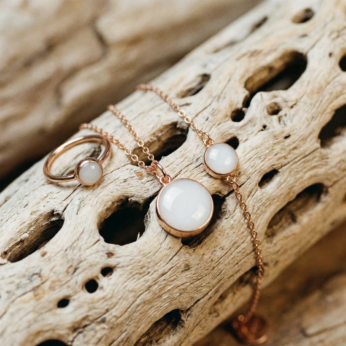 Colgante, anillo y pulsera en tono oro rosa con cabujones blancos sobre madera natural, joyería recuerdo para el destete.