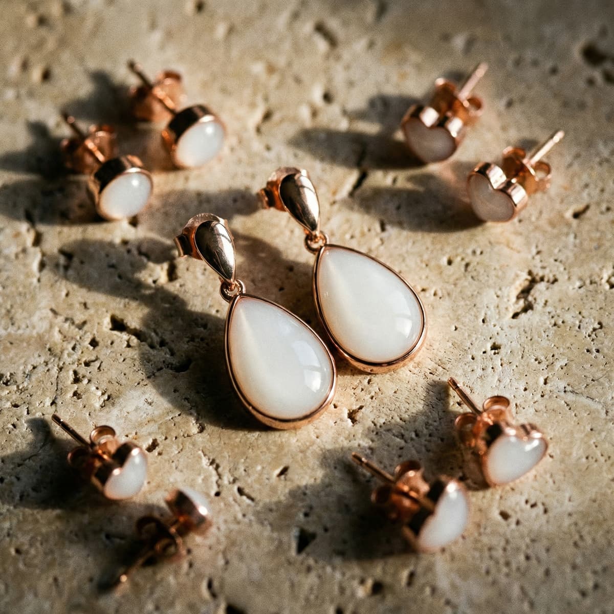 Pendientes en tono oro rosa con resina blanca presentados sobre una piedra texturizada, parte de un kit creación pendientes leche con diseño de gota y studs para recuerdo de leche materna.