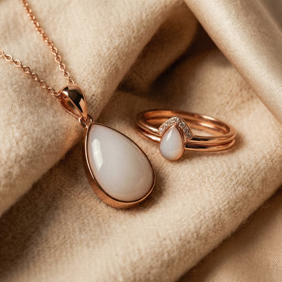 Colgante y anillo de oro rosa con piedra blanca en forma de lágrima sobre tela beige, joyería minimalista ideal como recuerdo destete respetuoso