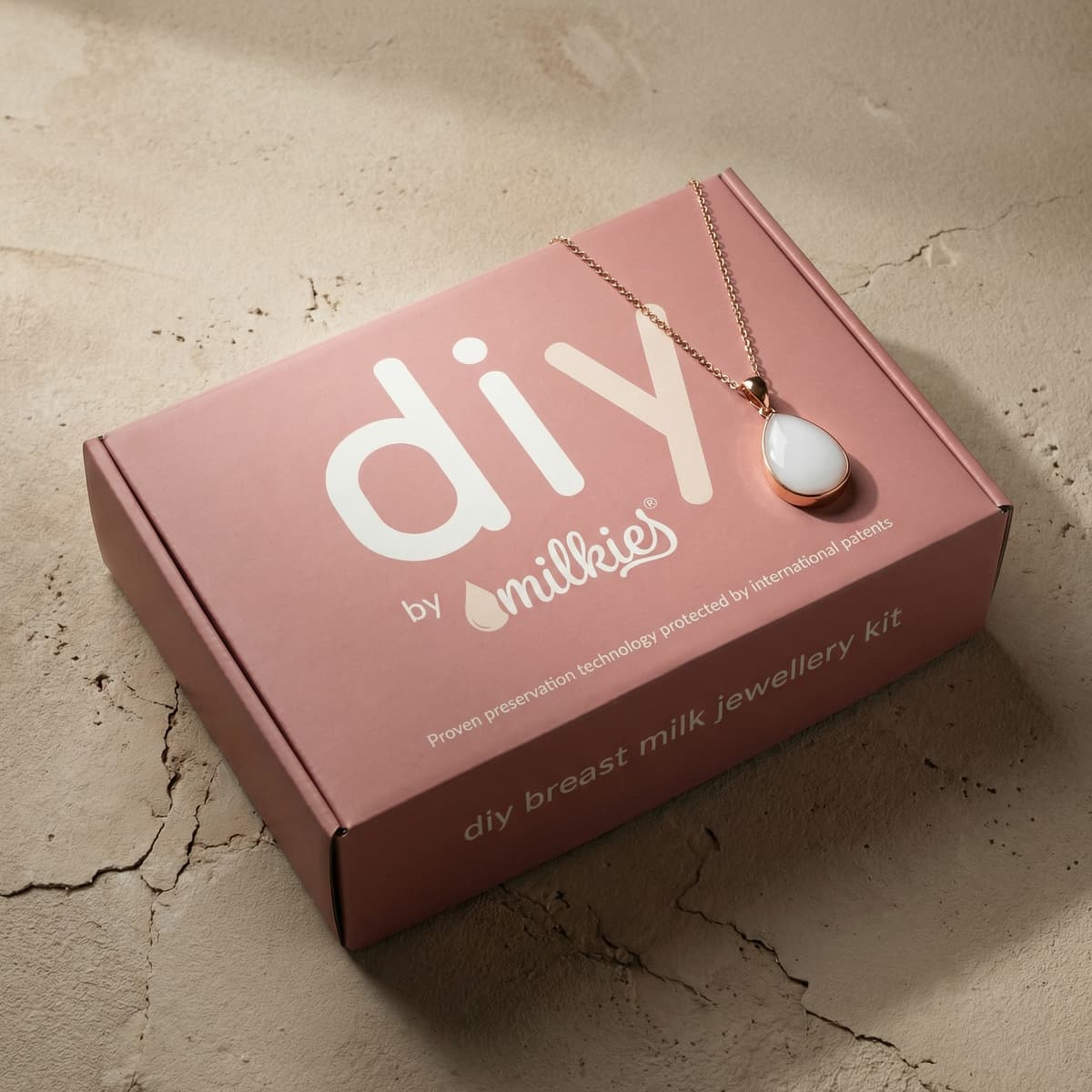 Kit DIY by Milkies para crear joyería con leche materna en casa, una idea de regalo lactancia, con caja rosa y colgante blanco con cadena dorada.