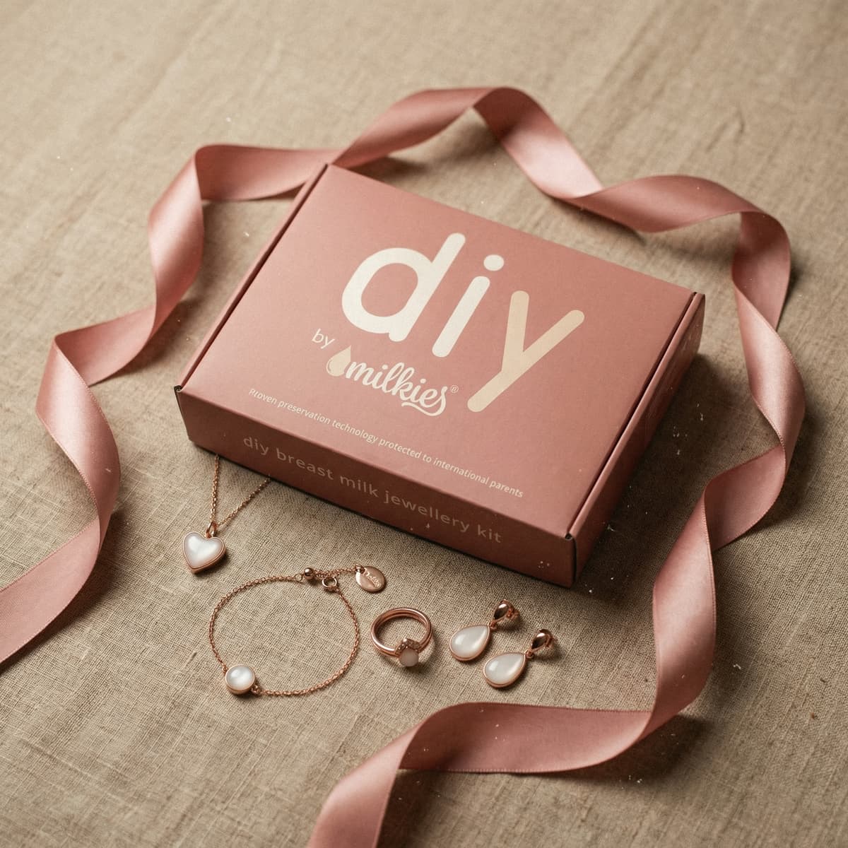 Kit DIY by Milkies de joyería con leche materna en caja rosa con cinta de raso y piezas (collar, pulsera, anillo y pendientes), una idea de regalo mama primeriza para crear un recuerdo en casa.