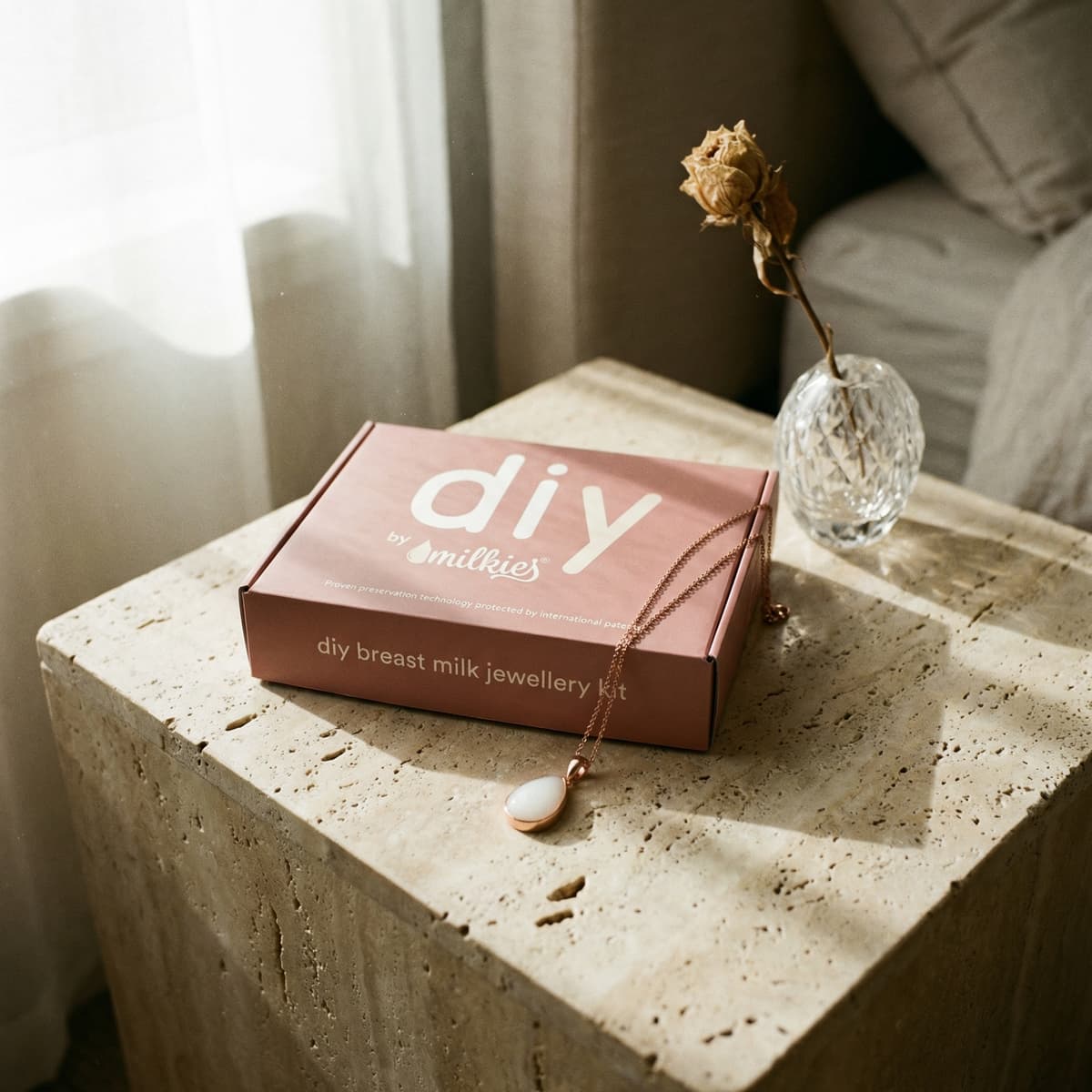 Kit DIY by MILKIES de joyería con leche materna en caja rosa sobre mesa de piedra, con colgante y flor seca, idea de regalo nacimiento bebe para crear un recuerdo personalizado en casa.