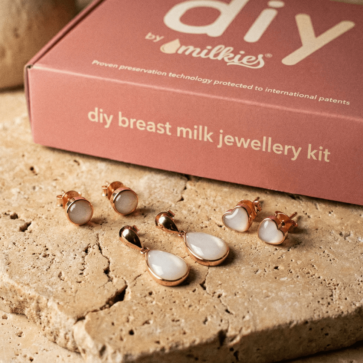 Aretes y colgante en tono oro rosado con resina blanca, un elegante set aretes leche materna sobre piedra natural junto a la caja del kit de joyería “DIY by Milkies”.