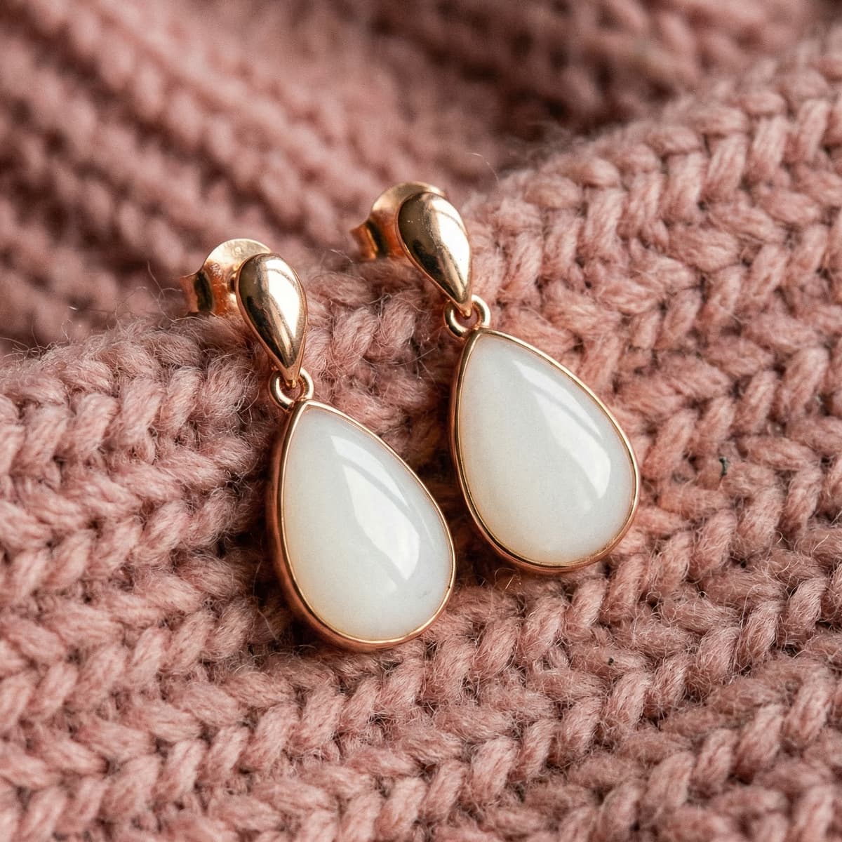 Aretes en forma de gota con resina blanca preservada, parte de un set aretes leche materna con marco dorado rosado, colocados sobre una manta tejida rosa.