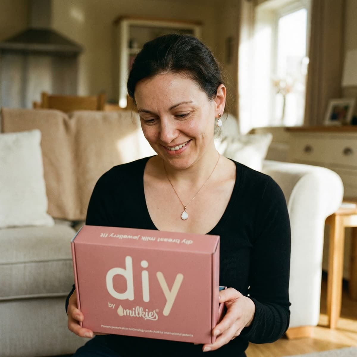 Madre sonriente en casa sosteniendo una caja DIY by MILKIES, ideal para crear un recuerdo personal con un set colgante leche materna y tecnología patentada de preservación.