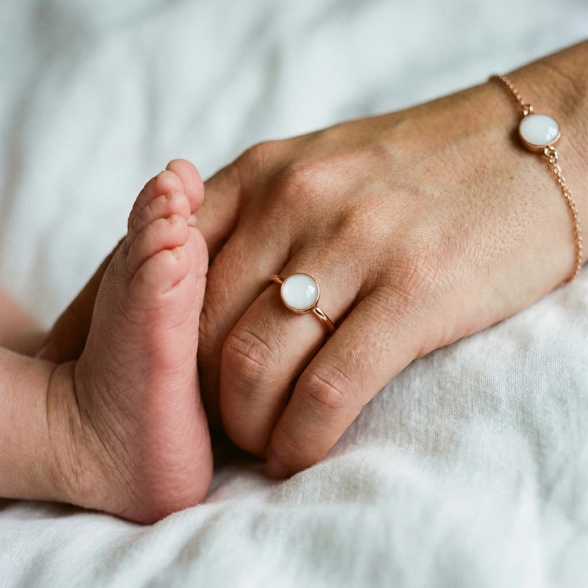 Madre sostiene el pie de su bebé y muestra un anillo y una pulsera con piedra blanca, inspiración para hacer joyas leche materna caseras como recuerdo artesanal.