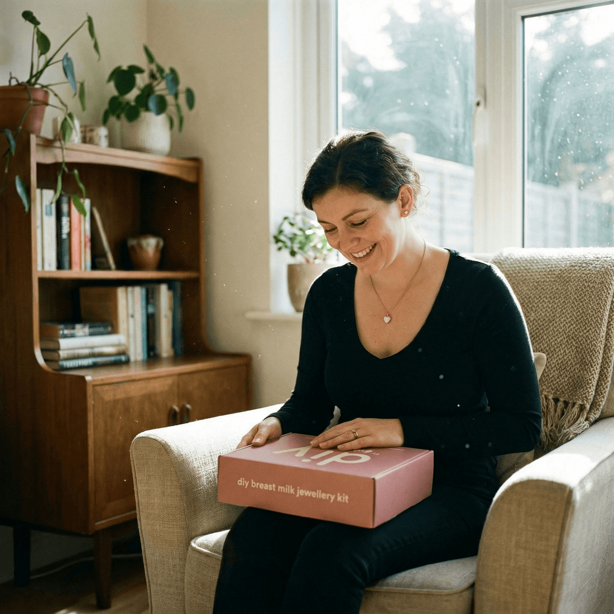 Madre sonriente en casa abriendo una caja rosa de DIY by MILKIES, mostrando por qué elegir un kit completo joyas leche materna para crear un recuerdo íntimo y artesanal en casa.