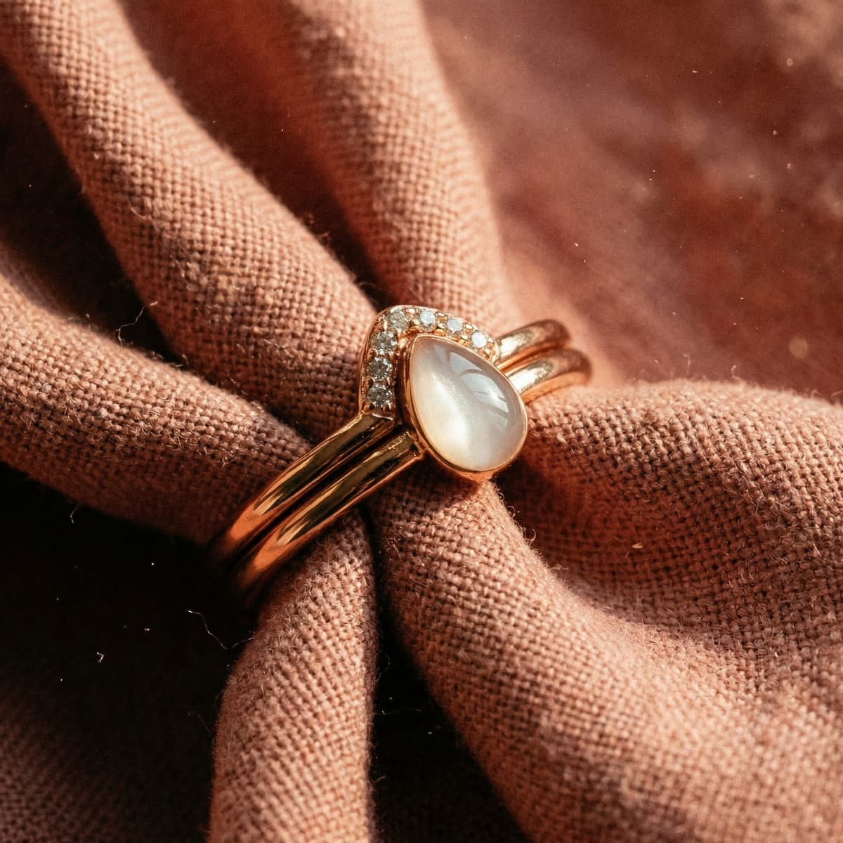Anillo de oro rosa con piedra blanca en forma de lágrima y halo de circonitas sobre tela, ejemplo de kit hacer anillo leche materna para crear un recuerdo artesanal en casa.
