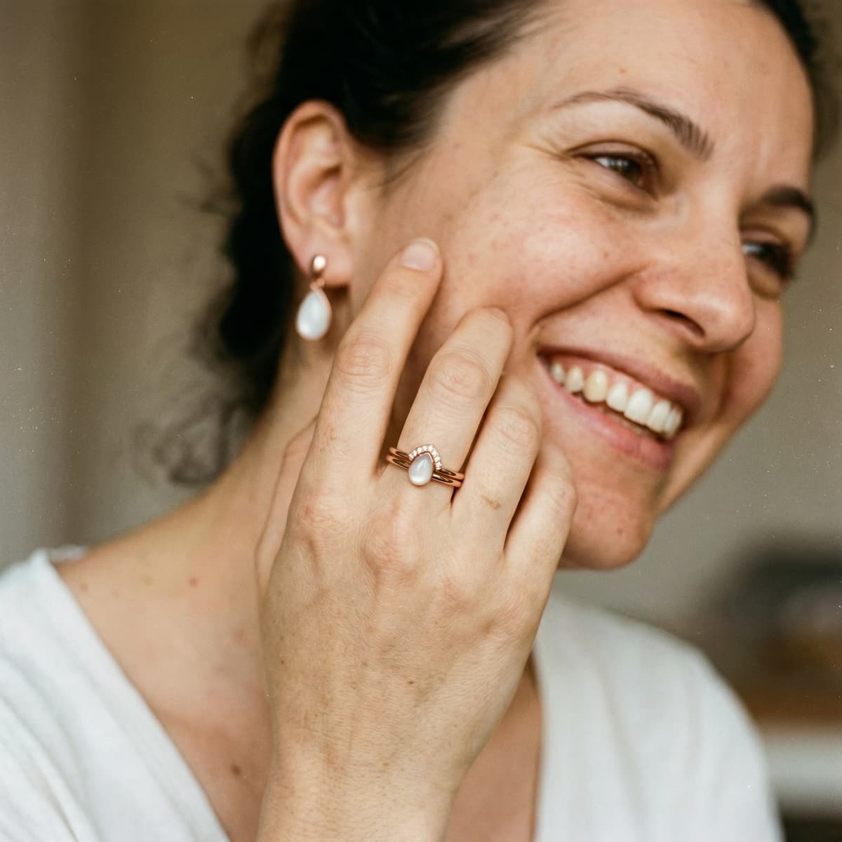 Mujer sonriendo con anillo de recuerdo con piedra blanca y pendientes a juego, mostrando por qué elegir un kit hacer anillo leche materna de DIY by MILKIES para crear en casa una joya sentimental con acabado elegante.